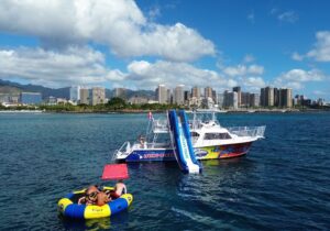 Living Ocean Tours boat with a waterslide, trampoline, and lily pad and Honolulu in the background