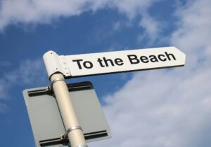 white sign that says To the Beach with the sky in the background